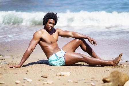 Smiling black man resting on sandy beach near sea