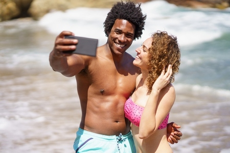 Happy diverse couple taking selfie on beach