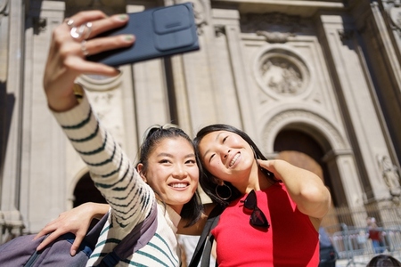 Cheerful Asian women taking selfie against historic building