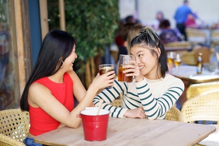 Cheerful Asian friends clinking glasses of drinks in cafe