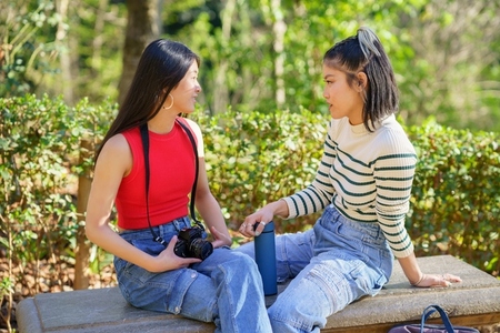 Calm Asian women chatting on bench during trip