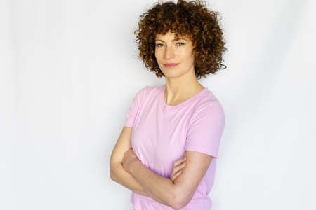 Confident woman with curly hair with crossed arms against white background