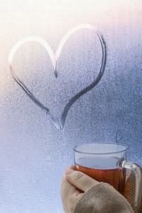 Close up hands cupping hot apple cider below heart shape on wet window