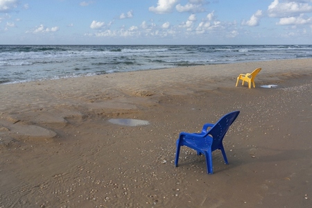 Plastic chairs on wet sandy ocean beach