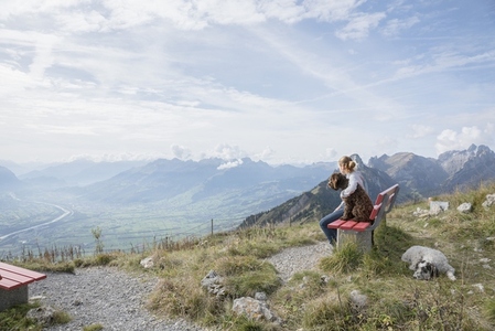 Girl with dogs sitting on bench enjoying scenic