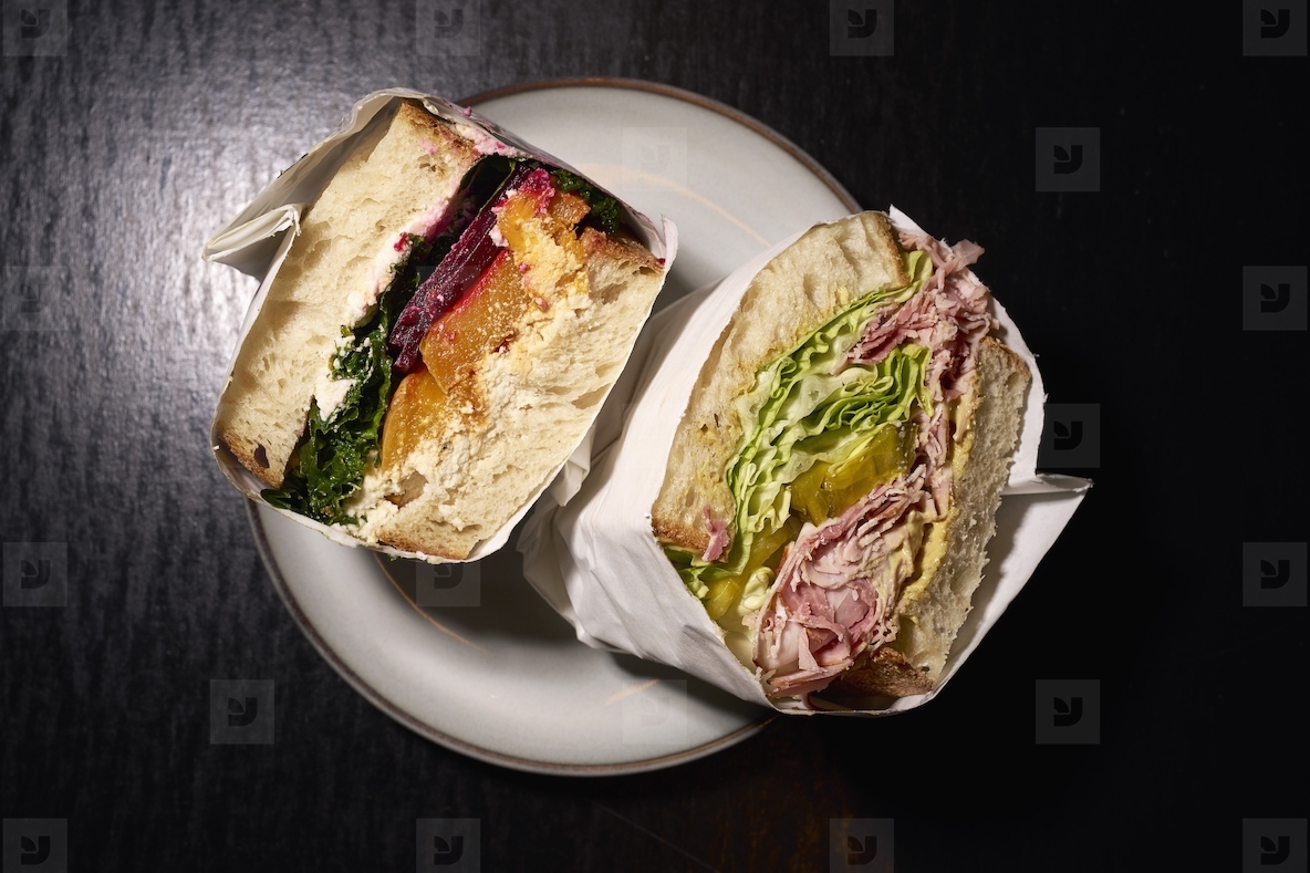 Still life gourmet sandwich halves wrapped in paper on plate