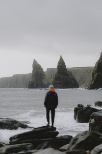 Man looking at rock formations and cliffs along ocean coastline