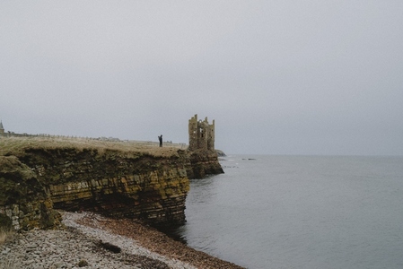 Man on cliff by abandoned castle over sea Keiss