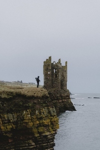 Tourist on cliff by castle ruins over sea