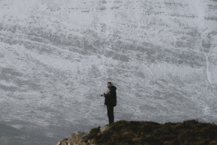 Photographer standing on hill below snowcapped mountain