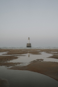 Lighthouse on sea beyond tide pools on beach