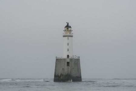Lighthouse in sea under overcast sky