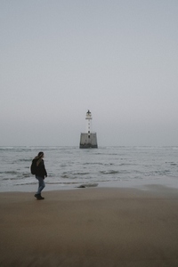 Woman walking on ocean beach with lighthouse
