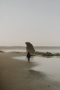 Woman walking on wet sand ocean beach at sunset