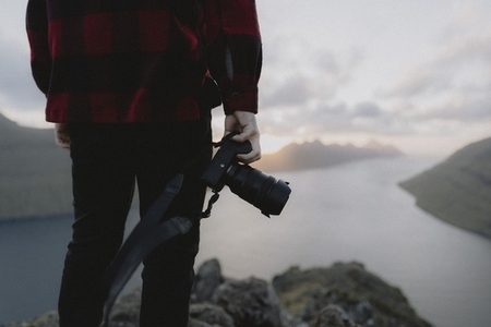 Photographer holding SLR camera on hill overlooking sea