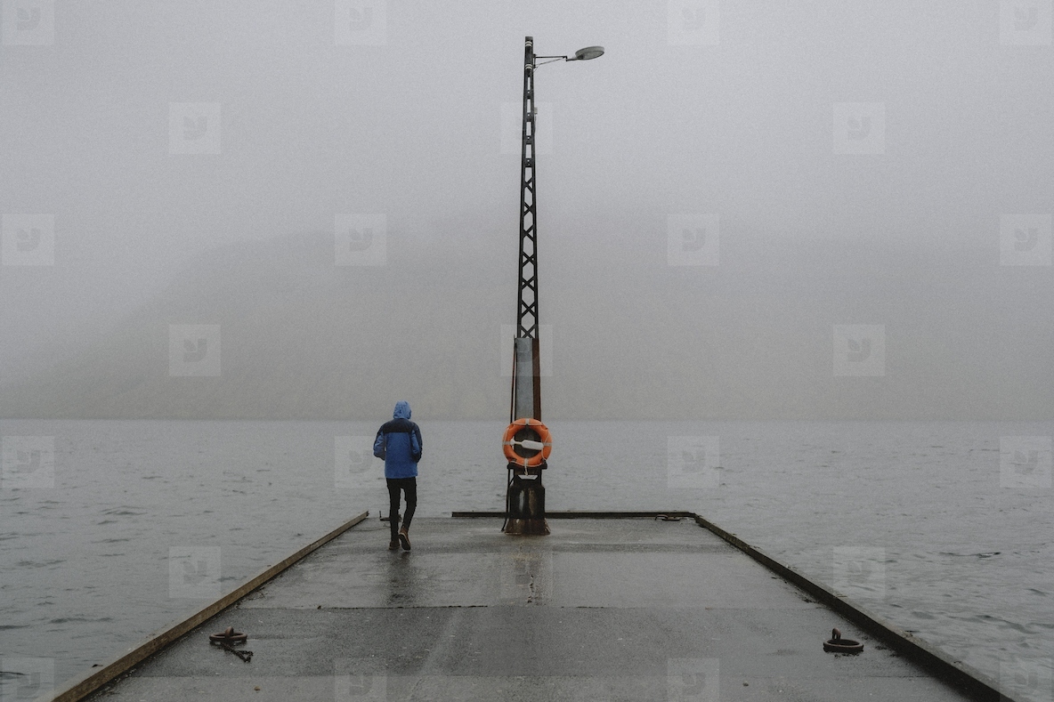 Man standing in rain on jetty overlooking foggy ocean