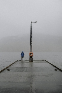 Man standing in rain on jetty overlooking foggy ocean 02