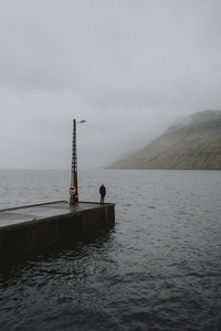 Man standing on rainy foggy jetty over ocean