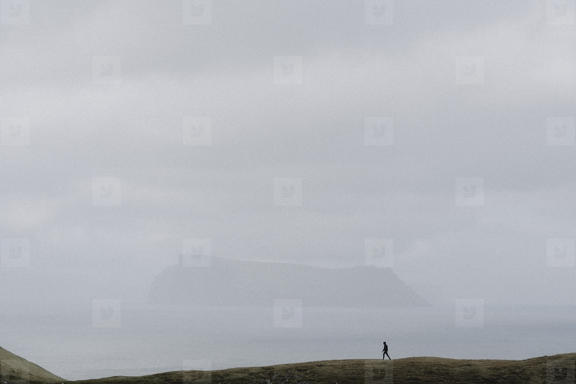 Man in distance walking on cliff over foggy ocean