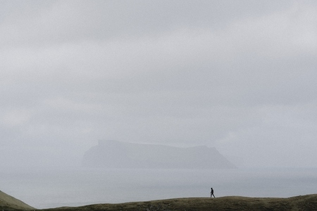 Man in distance walking on cliff over foggy ocean