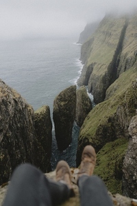 POV hiker sitting on cliff above sea stacks over ocean