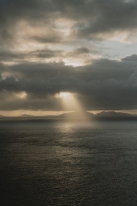 Sunbeam in dramatic sky over tranquil ocean at sunset