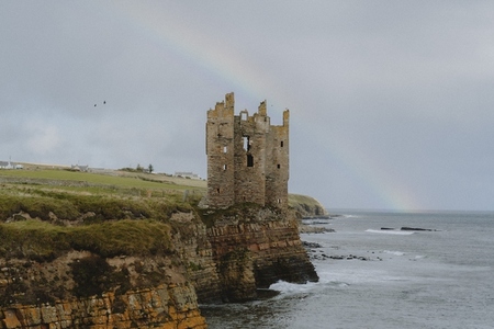 Rainbow behind castle ruins on cliff above ocean