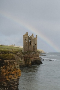 Rainbow behind castle ruins on cliff over ocean