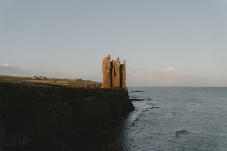 Sunlight over castle ruins on cliff above ocean