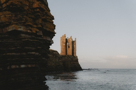 Sunlight over castle ruins on cliff above ocean 02
