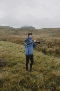 Male photographer using SLR camera on grassy hill