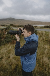 Male photographer using SLR camera in grassy field 02