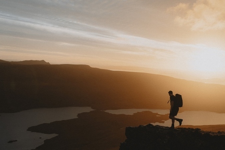 Silhouetted hiker on mountain overlooking idyllic sunset view