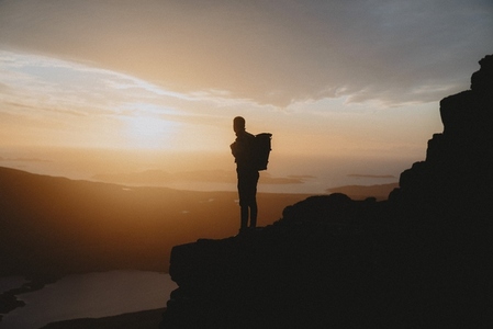 Silhouetted hiker standing on mountain looking at dramatic sunset sky