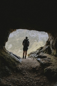 Male hiker standing in entrance of rugged mountain cave