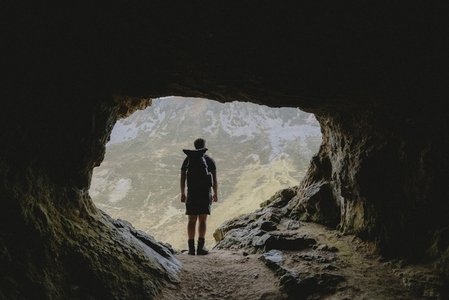 Male hiker standing in entrance of rugged mountain cave 02