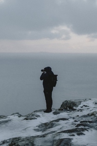 Photographer hiking photographing ocean from snowy cliff