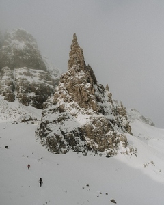 Hikers climbing mountain slope below snow covered rock formation