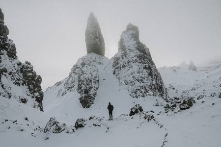 Hiker standing below tall snow covered mountain rock formation
