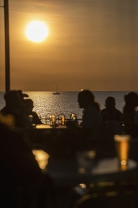 Silhouetted people drinking beer on waterfront patio with ocean view at sunset