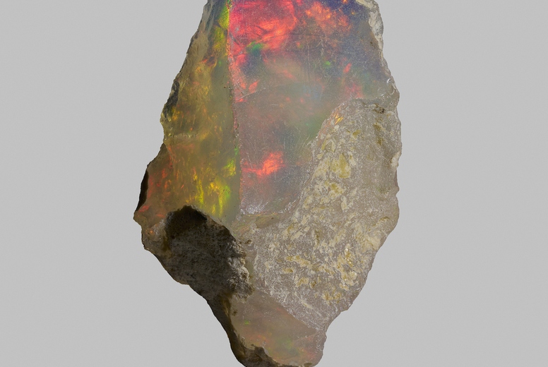 Close up iridescent multicolored welo opal on gray background 02