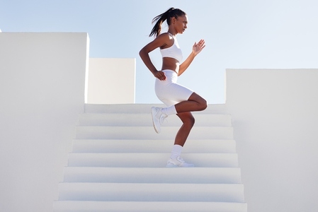 Young slim woman running down stairs while exercising outdoors  Side view of fit female running down on stairs