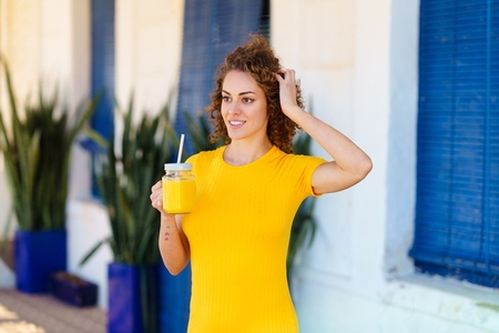 Cheerful woman with juice touching hair on street