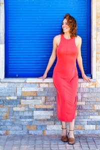 Woman in sleeveless red dress standing near bright wall