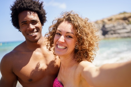Content diverse couple taking selfie on coast of sea