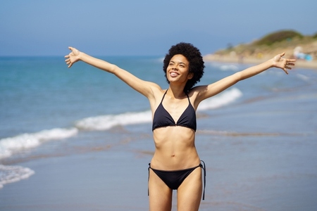 Gleeful black woman in bikini standing near sea