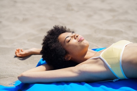 Relaxed ethnic lady sunbathing on sandy shore on summer day
