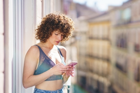 Young female in bra and jeans with curly hair while browsing smartphone