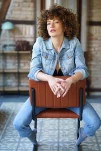 Serious young woman wearing denim jacket sitting on leather chair
