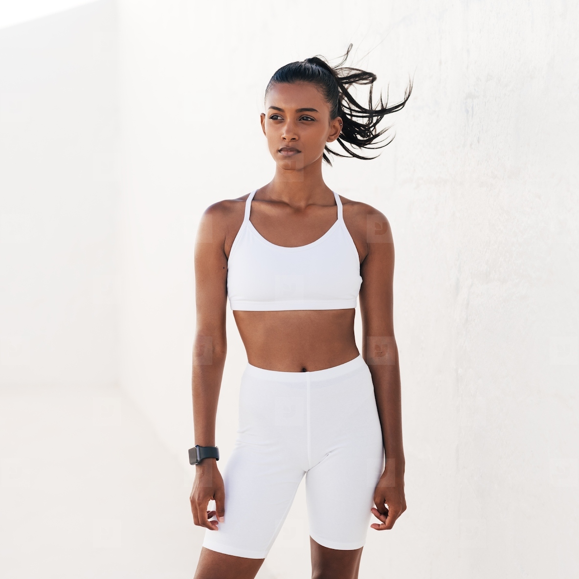 Confident sportswoman in white fitness clothes standing outdoors and looking away